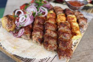 Close-up of grilled kebabs with roasted potatoes, onions, and sauce, served on flatbread.