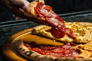 Fresh pepperoni pizza slice being lifted from a wooden board by hand. Tasty and mouth-watering dinner option.